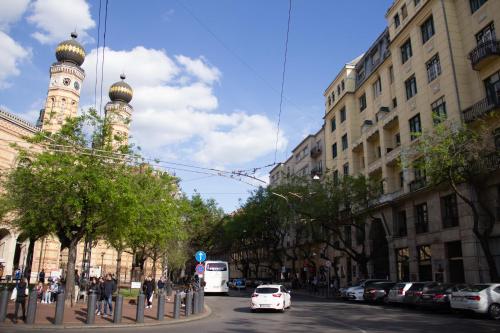 a white car driving down a city street with a clock tower at Luxury Downtown 3 Bedroom Apartment by Synagoge with Beautiful View in Budapest