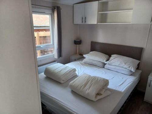 a white bed with two pillows on it with a window at Boshuis met grote tuin I Vakantiepark met Zwembad in Hoenderloo