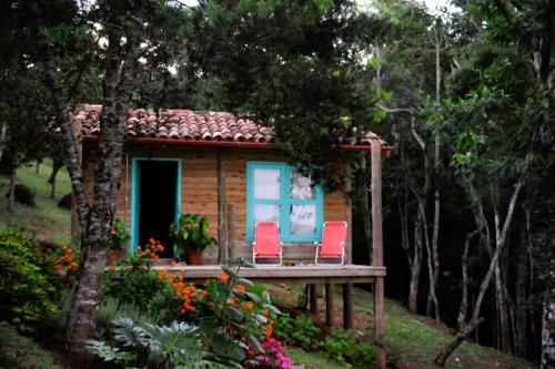 a small cabin with two red chairs on a porch at Chalé Paiol - Sítio Lajinha in Alagoa
