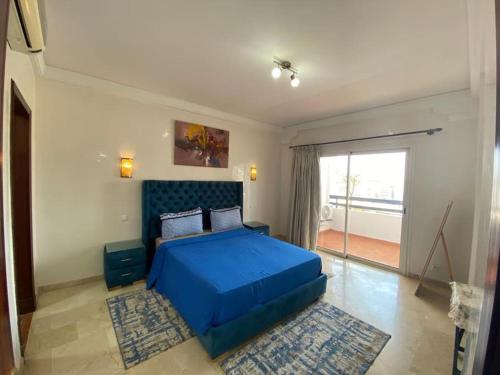 a bedroom with a blue bed and a large window at Marina Agadir Comfy Apartment in Agadir