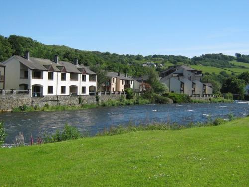 a river with houses next to a grassy field at Lakeland Village in Newby Bridge