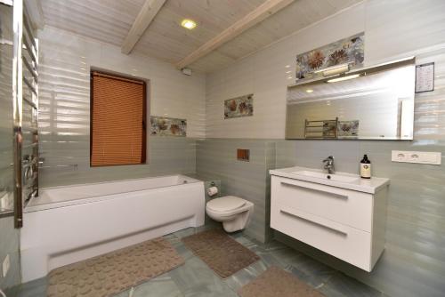 a bathroom with a tub and a toilet and a sink at Sodyba Gintaras in Priekulė