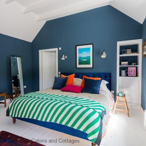 a blue bedroom with a bed with colorful pillows at The Bothy in Banchory