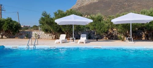 two white umbrellas and two chairs and a swimming pool at Koukouri Suites in Areopolis