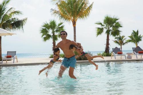 a man and two children playing in a swimming pool at Dreams Aventuras Riviera Maya - All Inclusive in Puerto Aventuras