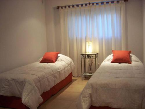1 dormitorio con 2 camas con almohadas rojas y ventana en Casa en Pinamar Alquiler en Pinamar