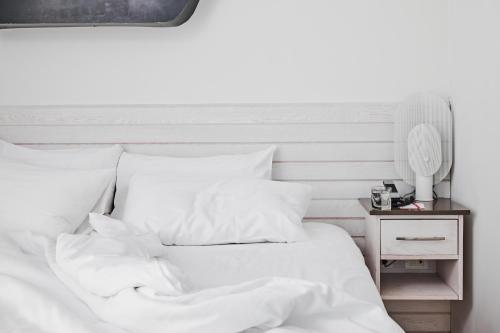 a white bed with white sheets and a night stand at Bungalow Hotel in Long Branch