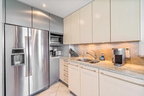a kitchen with white cabinets and a stainless steel refrigerator at The Noniluna Two - Sleeps 9 plus Pack N Play in Lahaina