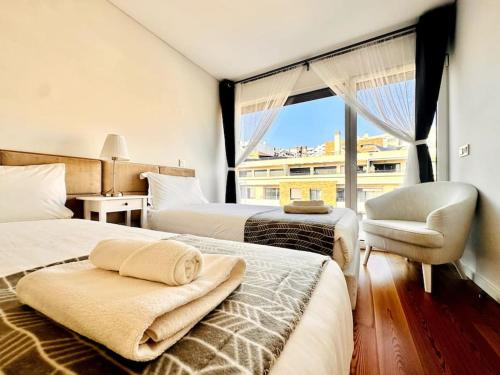 a bedroom with two beds and a chair and a window at Luz Benfica Apartment in Lisbon