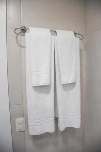 three white towels hanging on a towel rack in a bathroom at Jurerê Beach Village - Studio Vista Mar in Florianópolis