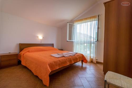een slaapkamer met een bed met oranje lakens en een raam bij Apartments by the sea Supetarska Draga - Gornja, Rab - 21380 in Rab