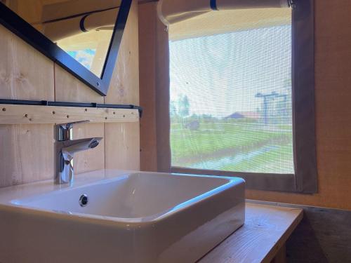 lavabo blanco en un baño con ventana en Luxury glamping with private bathroom near the Frisian waters, en De Veenhoop