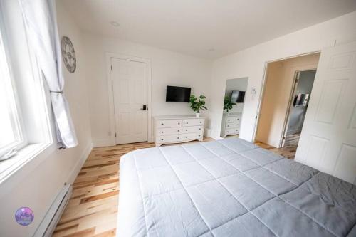 a white bedroom with a large bed and a tv at Le Petit Manoir - Quartz in Lac-Simon