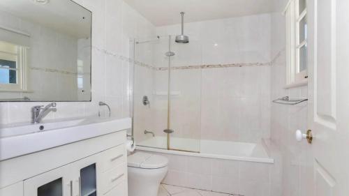 a white bathroom with a shower and a toilet and a sink at Reflections Yamba Lighthouse Cottages in Yamba