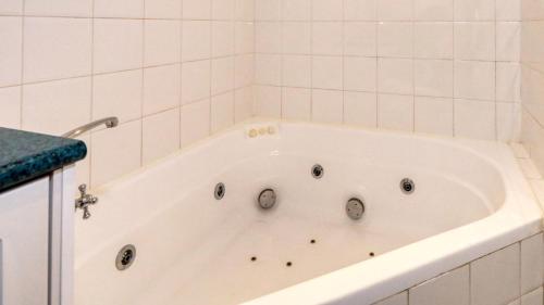 a white bath tub in a white tiled bathroom at Hilltop Motel in Broken Hill