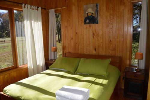 a bedroom with a bed with green sheets and a window at Cabañas Valle del Río in Curacautín