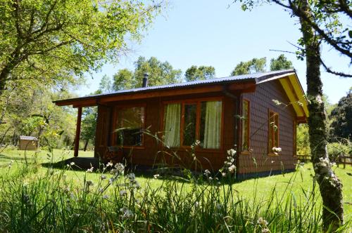 a small cabin in a field with trees and grass at Cabañas Valle del Río in Curacautín
