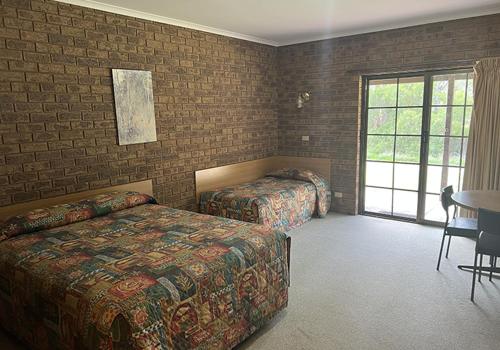 a bedroom with two beds and a table and a window at Tocumwal Early Settlers Motel in Tocumwal