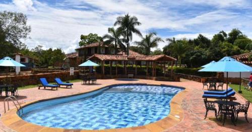 a swimming pool with chairs and umbrellas in front of a house at Hotel Finca Buenos Aires Barichara in Barichara