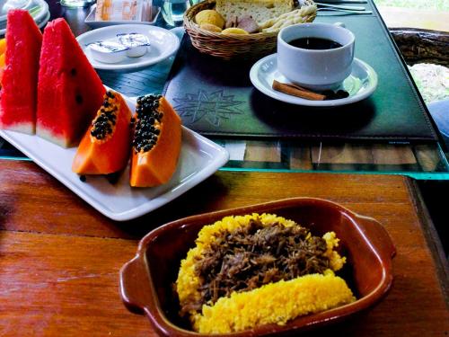 a table with a plate of fruit and a cup of coffee at Pousada Dos Artistas in Praia do Forte