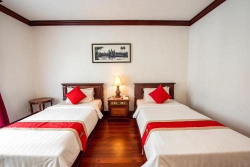two beds in a room with white walls and red pillows at Royal Crown Hotel & Spa in Siem Reap
