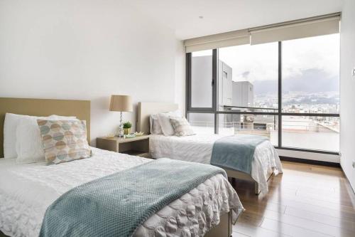 two beds in a bedroom with a large window at Luxury penthouse apartment in Quito