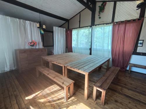 een houten tafel en banken in een kamer met ramen bij Pie lacuksa in Tīnūži