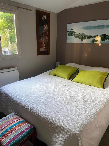 uma cama branca com almofadas verdes e uma janela em La Paillotte - 6 personnes em Pommeret