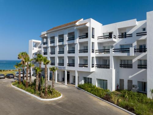 PLAYA DEL PACHA Suites Hotel في مارينا سمير: مبنى أبيض مع أشجار النخيل أمام المحيط