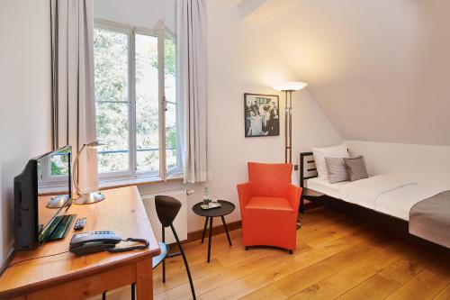 ein Wohnzimmer mit einem Bett und einem Schreibtisch mit einem Computer in der Unterkunft Hotel Mutterhaus Düsseldorf in Düsseldorf