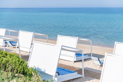 a row of white chairs on the beach at Pomegranate Wellness Spa Hotel in Nea Potidaea