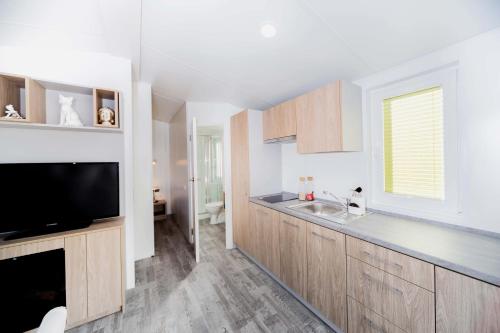 a kitchen with wooden cabinets and a tv and a sink at Randbøldal Camping & Cabins in Randbøl