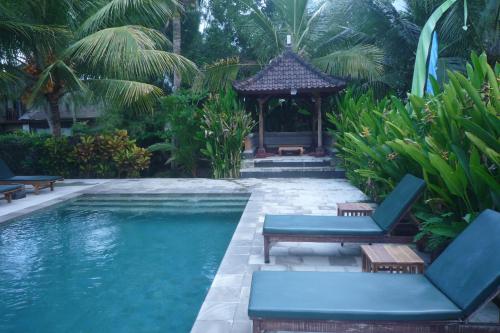 a swimming pool with chairs and a gazebo at Gerebig Bungalow in Ubud
