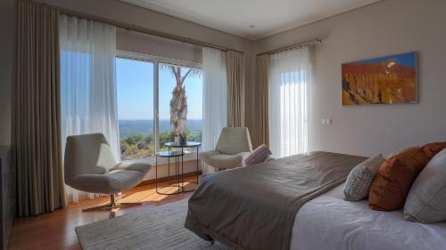 a bedroom with a bed and chairs and a large window at Villa Mebahel - Boliqueime in Boliqueime