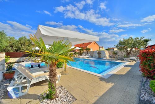 a pool with a white umbrella and chairs and a palm tree at Villa Dalmatina Zadar mit Pool in Zadar