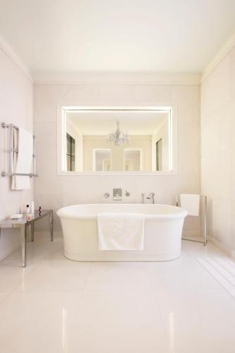 a white bathroom with a tub and a mirror at Hôtel Le Royal Monceau Raffles Paris in Paris