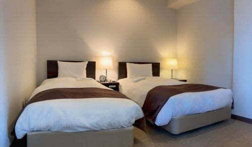 two beds in a bedroom with two lamps on at Shinjuku Sun Park Hotel in Tokyo
