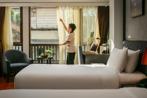 Kobieta patrzy przez okno pokoju hotelowego. w obiekcie Hanoi La Palm Premier Hotel & Spa w mieście Hanoi