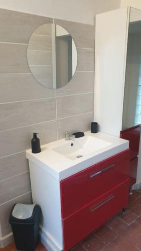 La salle de bains est pourvue d'un lavabo rouge et blanc et d'un miroir. dans l'établissement Bienvenue chez nous, à Guérigny