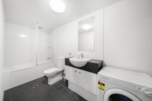 a white bathroom with a toilet sink and a washing machine at Oxygen Apartments in Brisbane