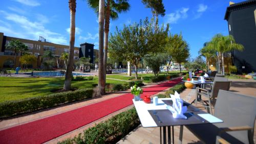 a park with tables and palm trees on a sidewalk at El Olivar Palace Marrakech All Inclusive, Aquapark & SPA in Marrakech