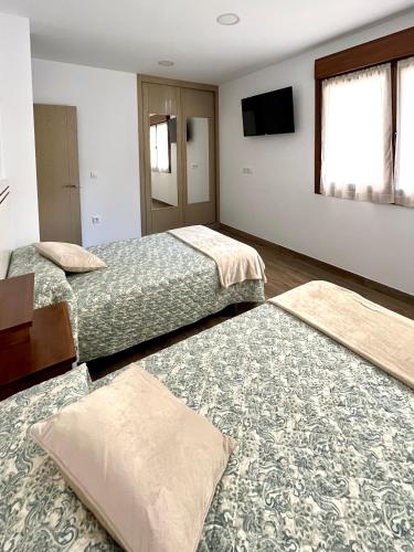 a hotel room with two beds and a flat screen tv at Apartamentos Valbuena in Potes