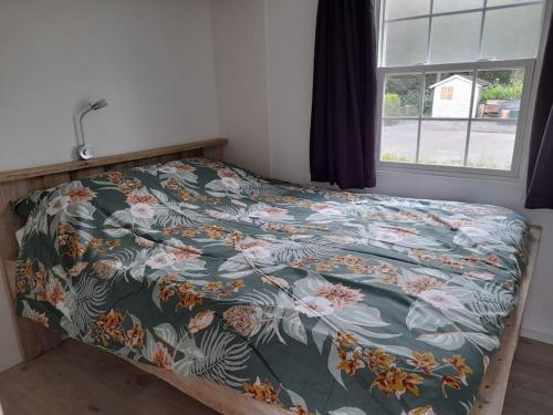 a bed with a floral comforter and a window at Natuurhuisje Oisterwijk in Oisterwijk