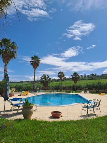 uma grande piscina com palmeiras ao fundo em Fattoria Manostalla Villa Chiarelli em Balestrate
