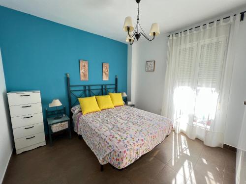 1 dormitorio con 1 cama con almohadas amarillas y pared azul en Apartamento Mirando al Mar, en Canet de Berenguer