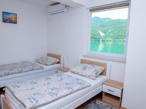 two beds in a room with a large window at Apartmani Jezero in Konjic