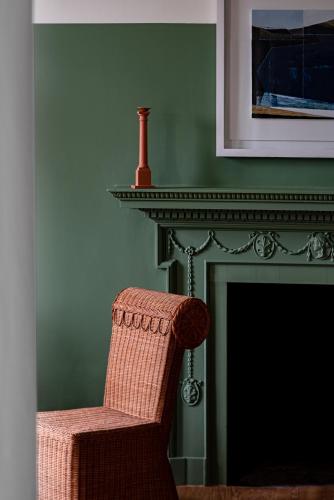 a chair sitting next to a fireplace with a red vase at Cowley Manor Experimental in Cheltenham