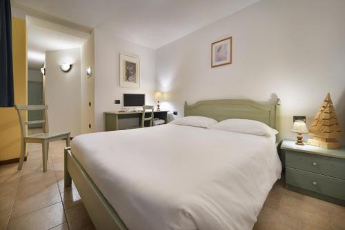 a bedroom with a large white bed and a desk at Hotel Tambò in Campodolcino