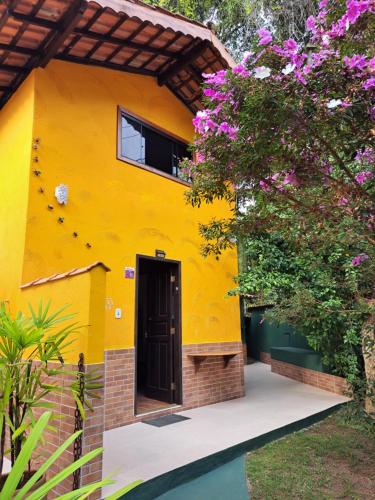 a yellow house with a black door and flowers at Recanto das Flores Lofts - Ilha Grande Rj in Abraão