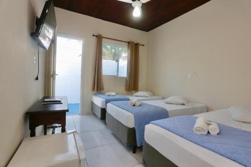 a room with three beds and a desk and a television at Pousada Albamar Guarujá in Guarujá